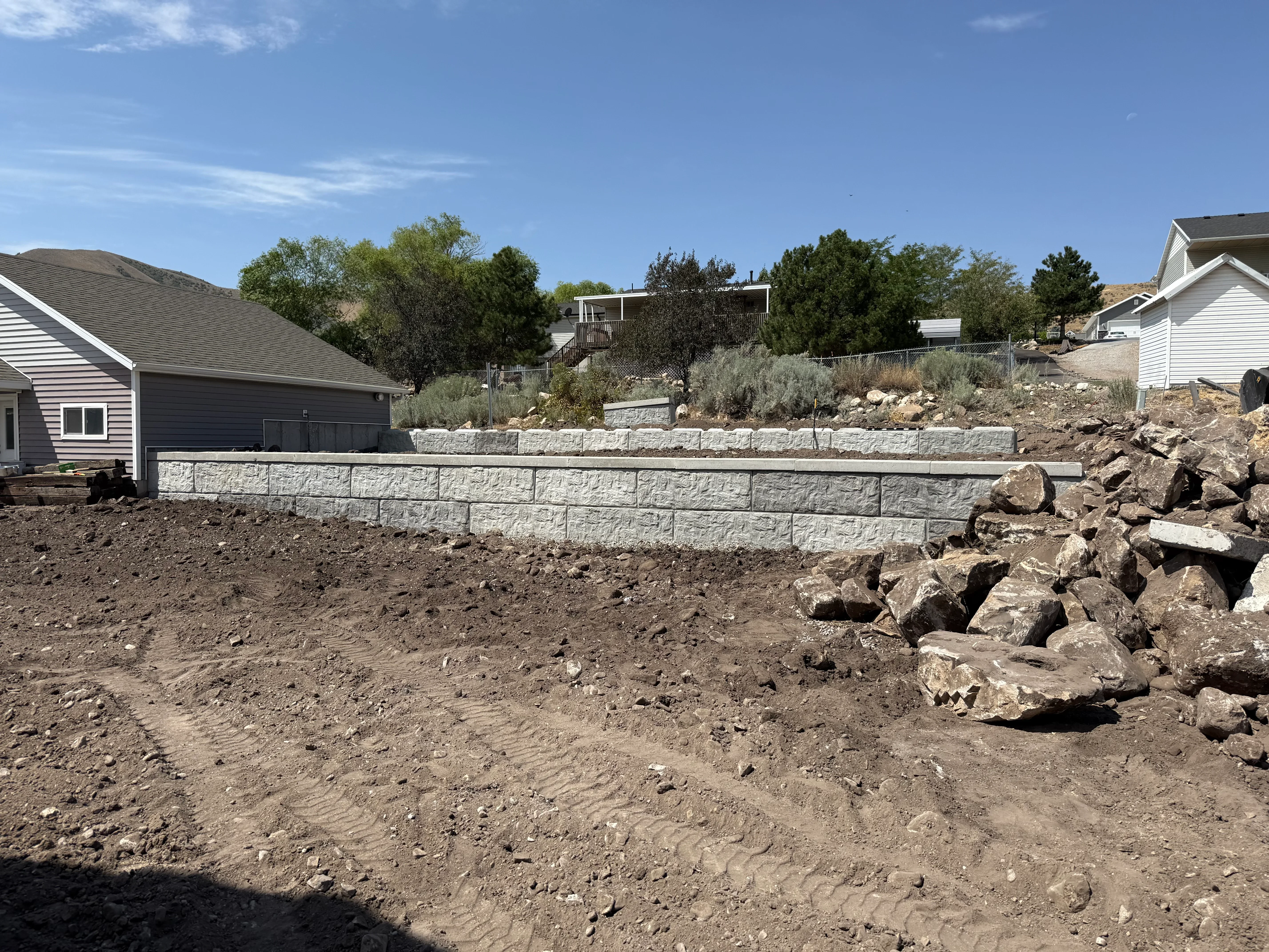 Stacked concrete retaining wall blocks on sloped residential lot with excavated earth