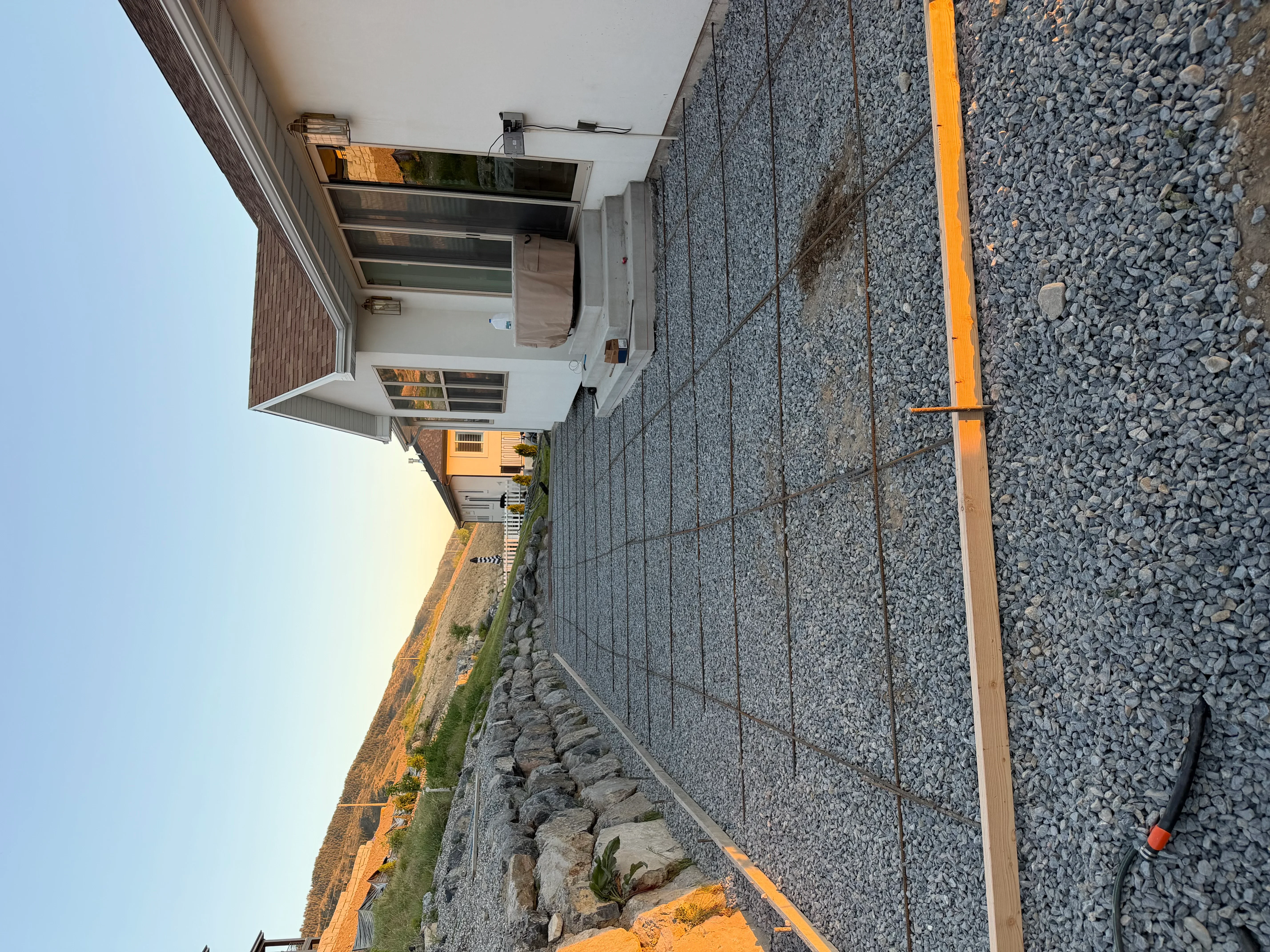 Concrete driveway with stacked stone retaining wall, gravel base, and yellow drainage pipe